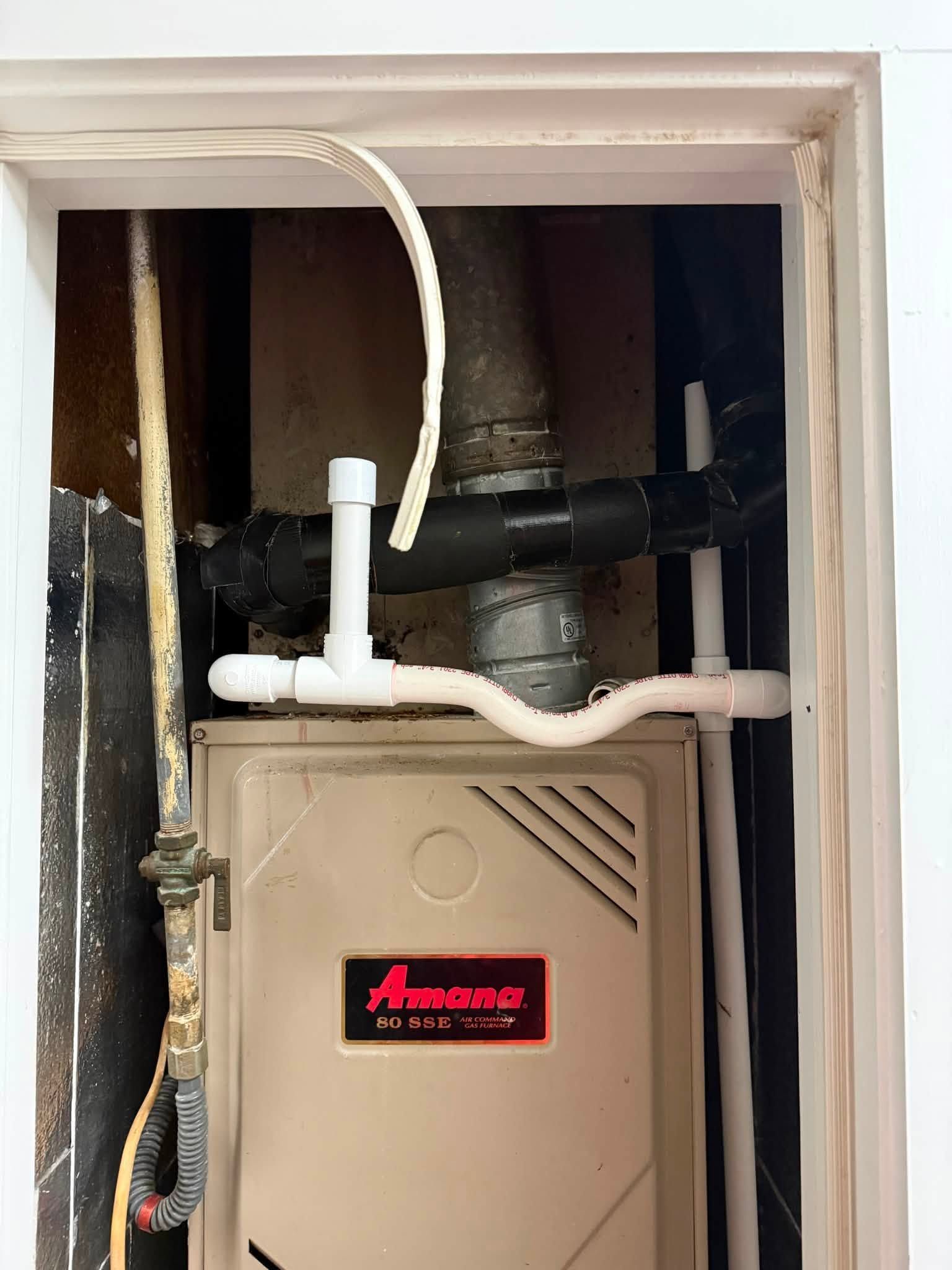 Open furnace compartment with white PVC and black duct pipes inside a wall cavity