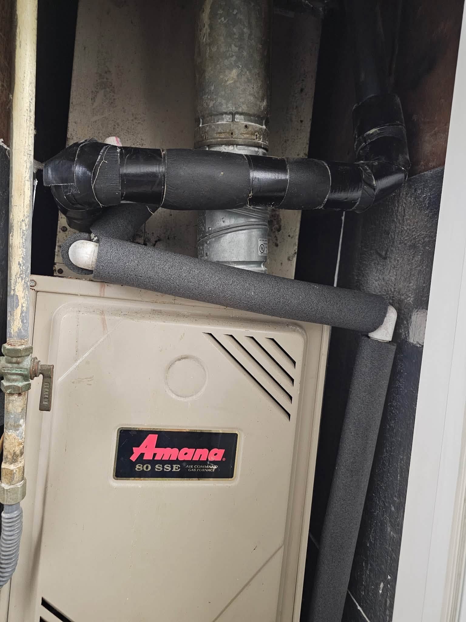 Beige furnace cabinet with black foam-wrapped pipes and ductwork in a utility closet
