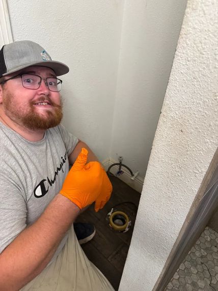 Person in orange gloves kneeling by a corner pipe opening in a utility area, holding a tool.