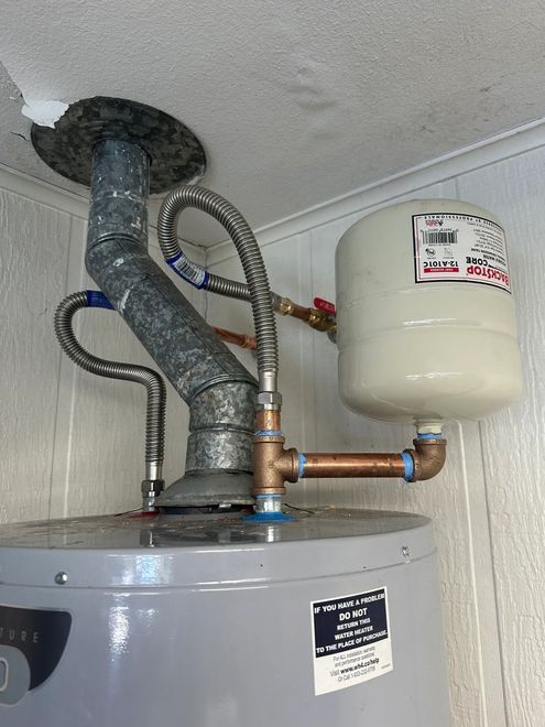 Water heater with connected vent pipes and expansion tank in a utility closet.