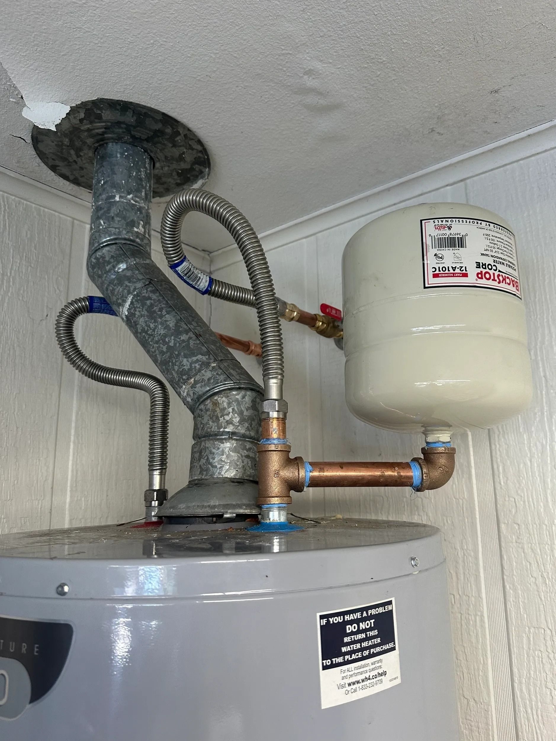 Water heater with vent pipe, expansion tank, and plumbing in a utility closet.