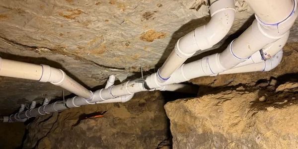 White pipes and fittings run along a rough cave-like stone ceiling and wall.