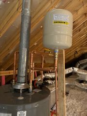 Water heater and expansion tank installed in an attic with exposed insulation and ductwork.