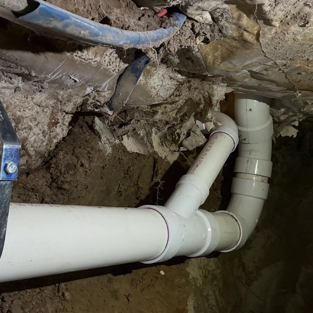 White PVC pipes joined in a muddy trench beside a rough stone wall
