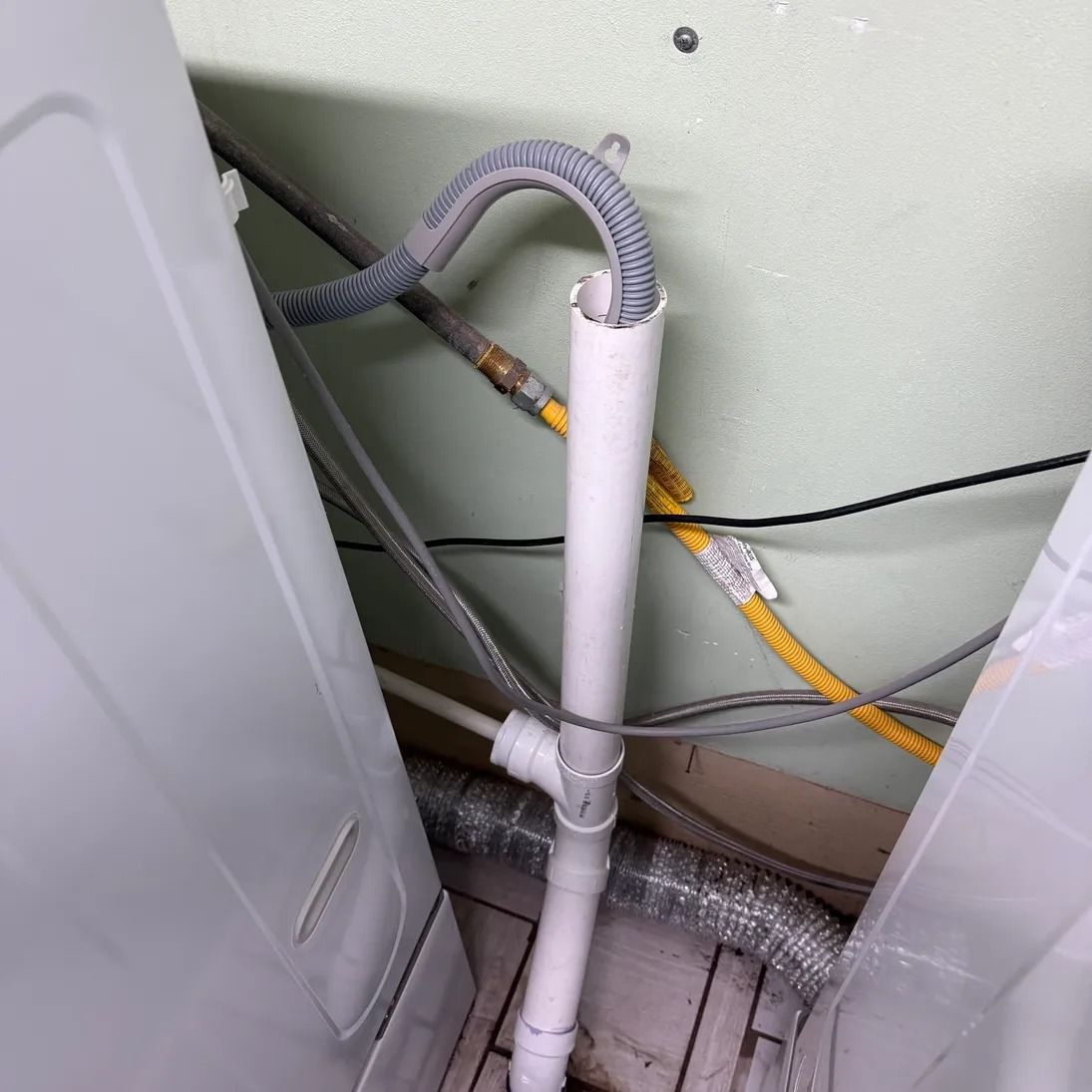 White PVC pipe and gray hoses running behind appliances in a tight utility space