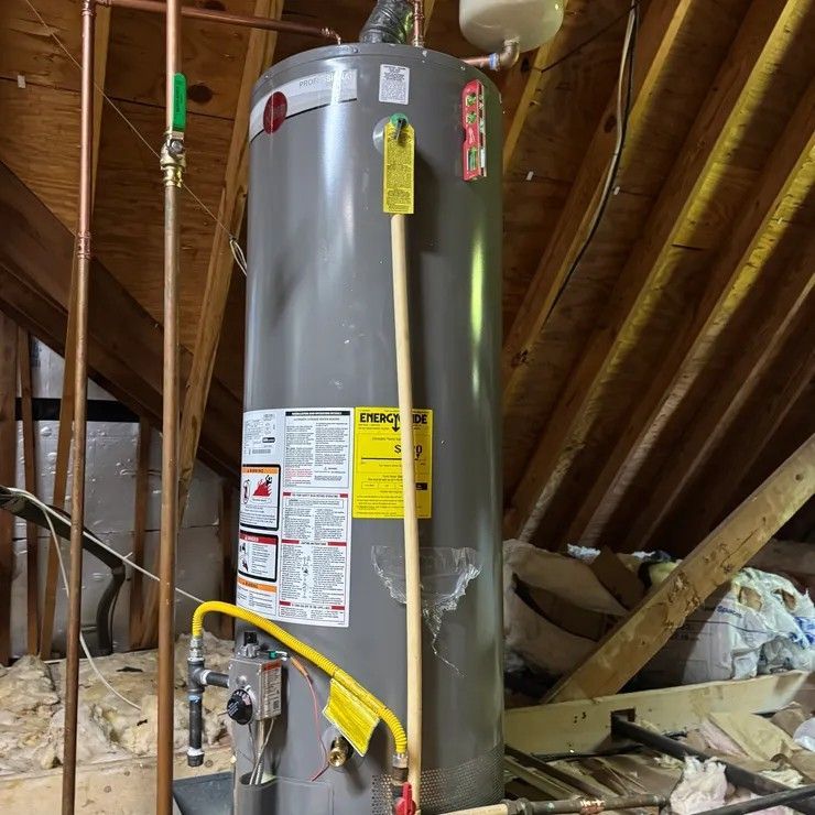 Gray water heater in an unfinished attic with exposed rafters and insulation.