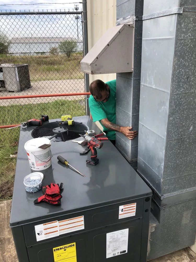 Technician crouches beside rooftop HVAC unit, working on wiring near a metal vent.