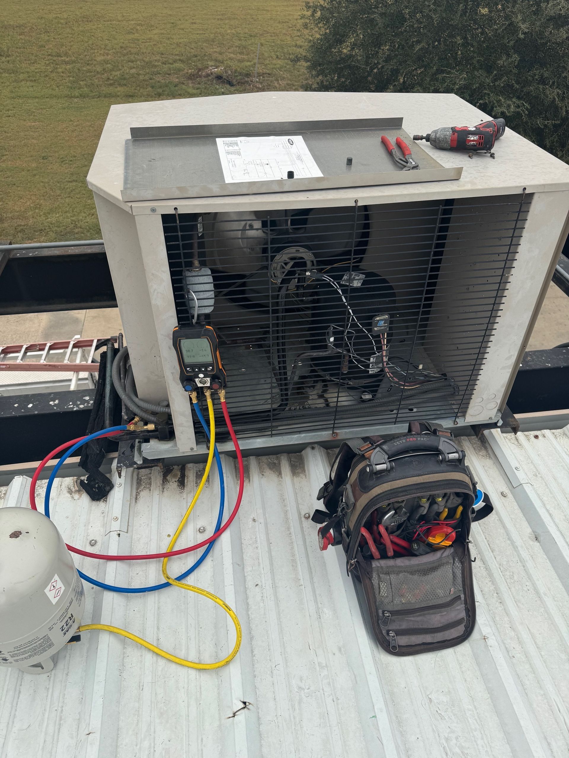 HVAC unit being serviced on a rooftop; gauges connected, tools nearby, overcast.
