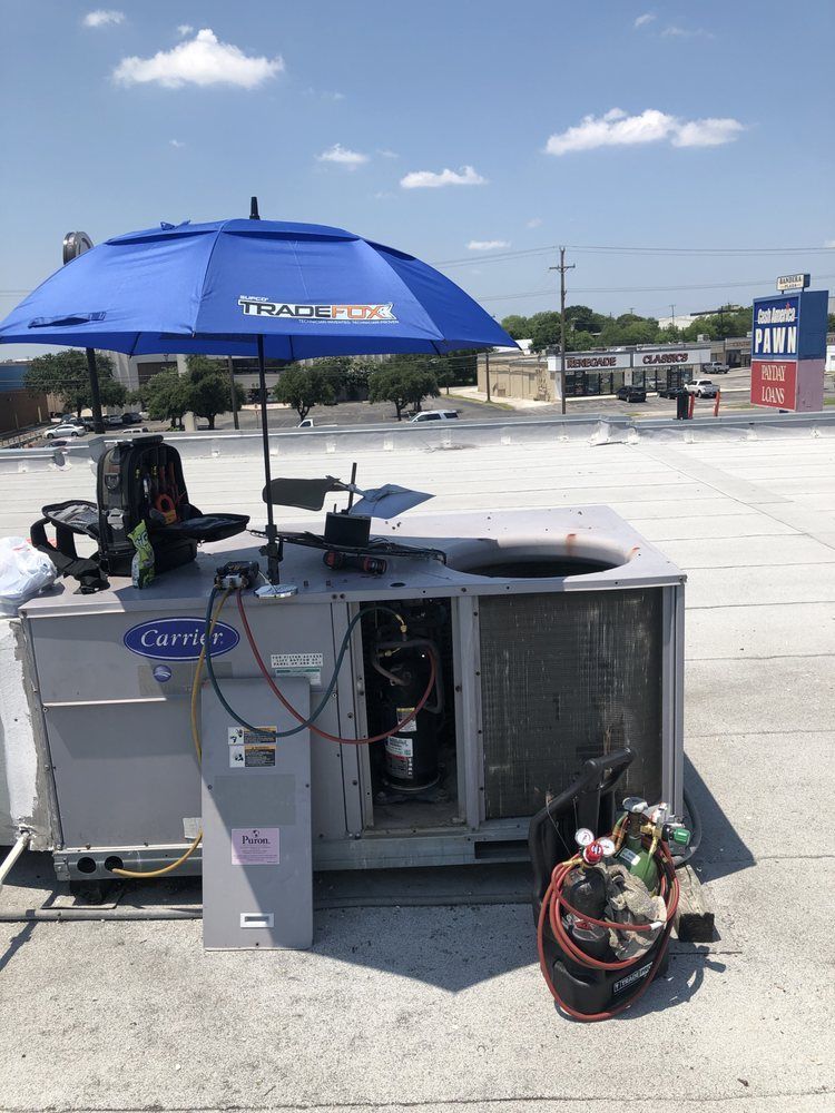 A blue umbrella is sitting on top of an air conditioner on a roof.