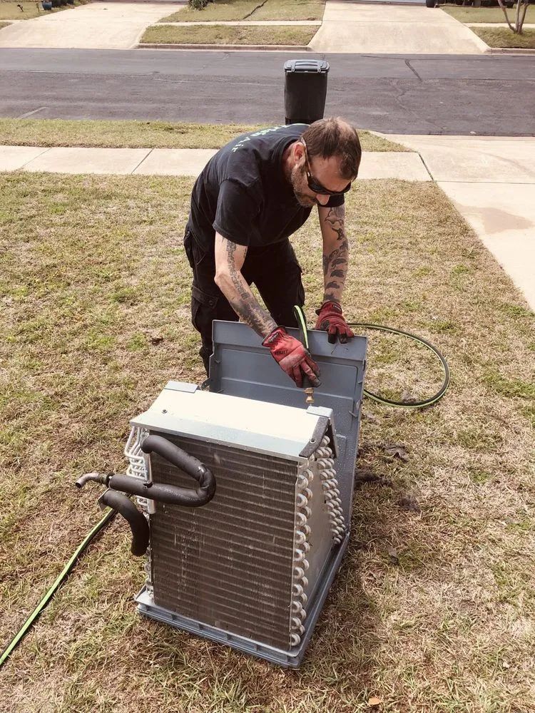 Person in gloves adjusts an outdoor HVAC unit in a front yard.
