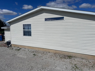 Exterior view of a cream-colored vinyl-sided house with a gravel ground, a small window, and a rectangular transom window.
