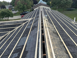 An unfinished residential roof featuring dark underlayment, parallel wooden battens, and an open central ridge vent.