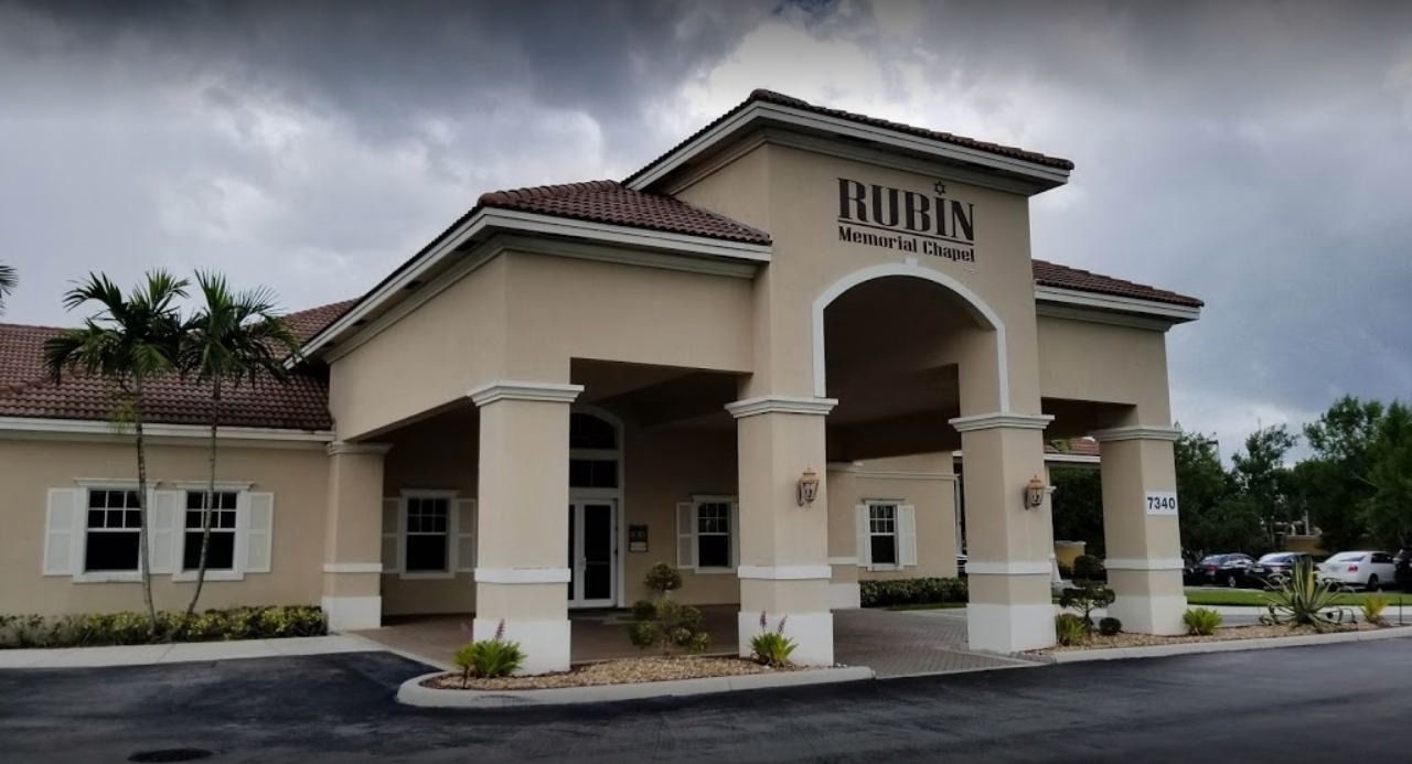 Front entrance of a beige building with columns and a covered driveway under cloudy skies