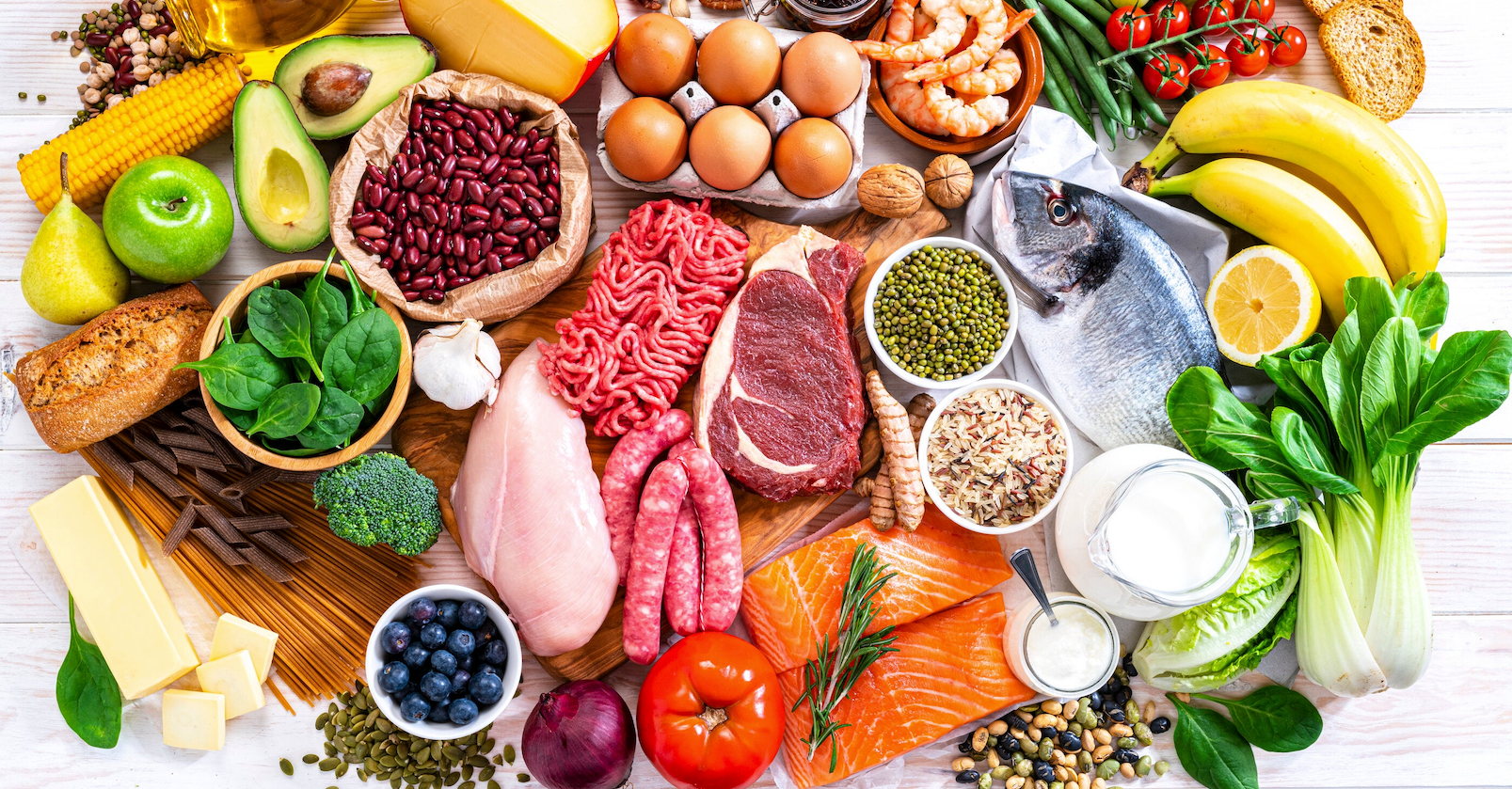 Assortment of colorful, fresh food: fruits, vegetables, meat, eggs, beans, dairy, seafood, and grains.