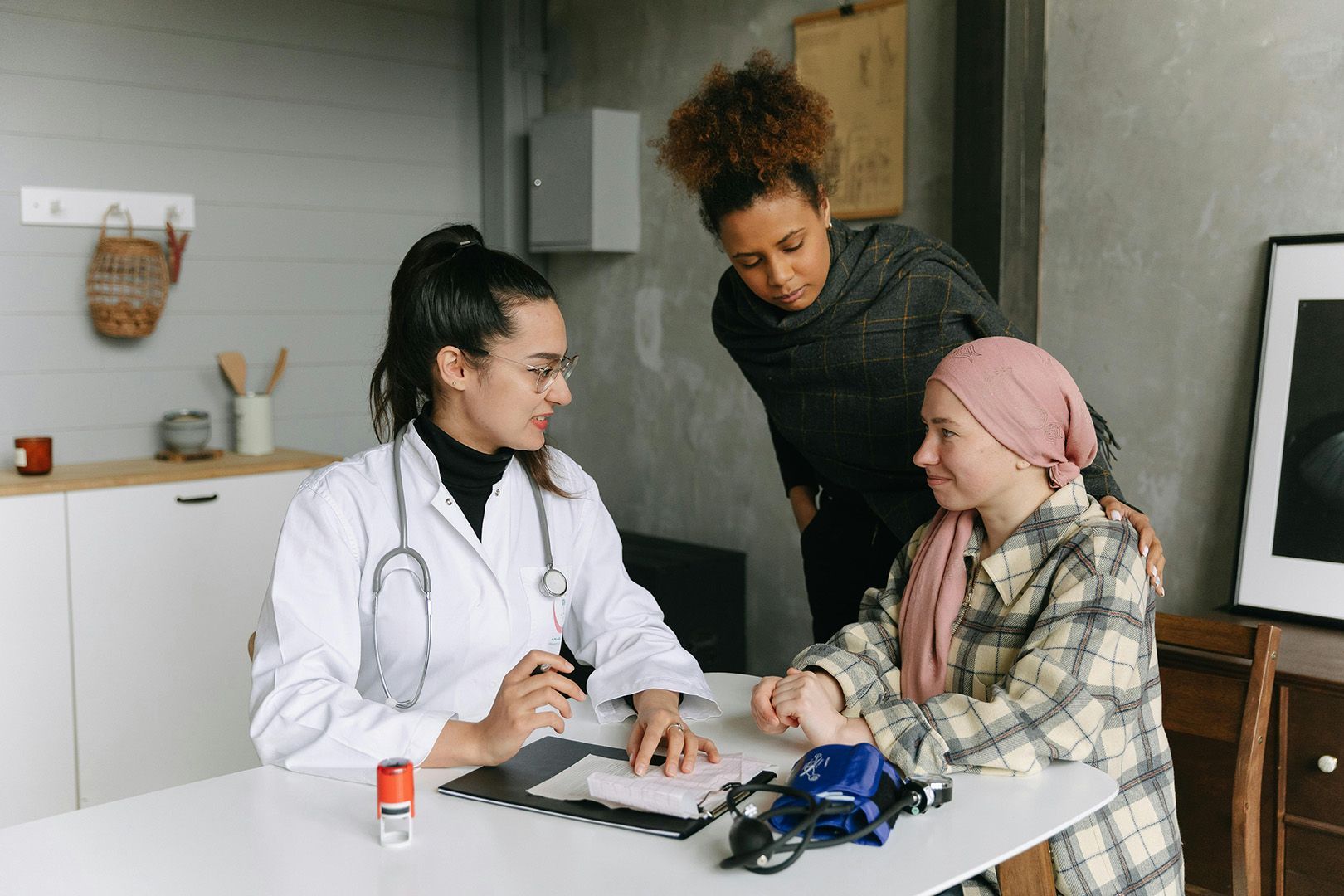 Doctor talking with a child wearing a head covering and an adult in a medical office.