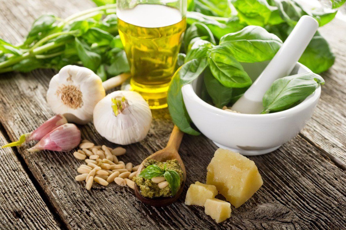Pesto ingredients: Basil, garlic, pine nuts, Parmesan, and olive oil, on a wooden surface.