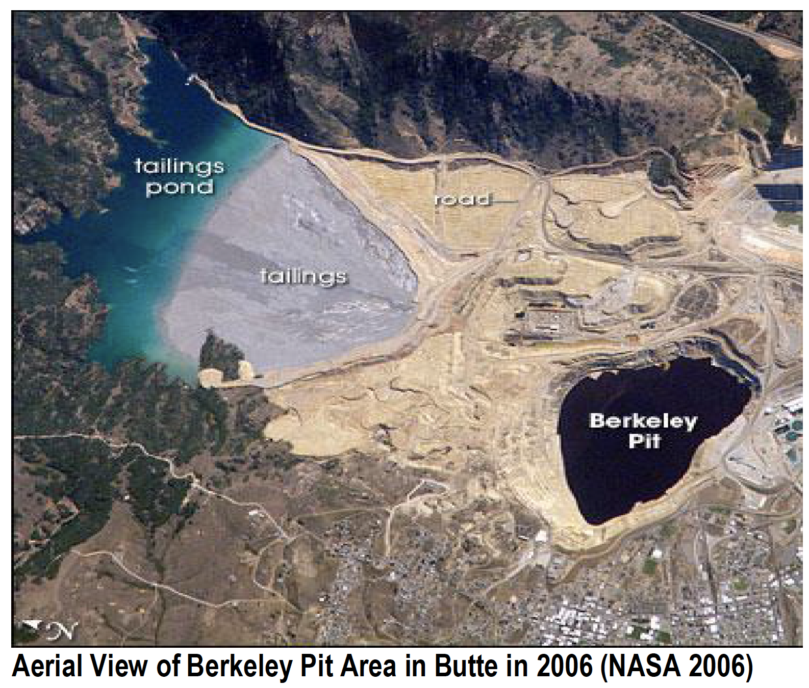 Aerial view: Berkeley Pit in Butte, Montana, with tailings pond and surrounding areas in shades of brown, gray, and blue.