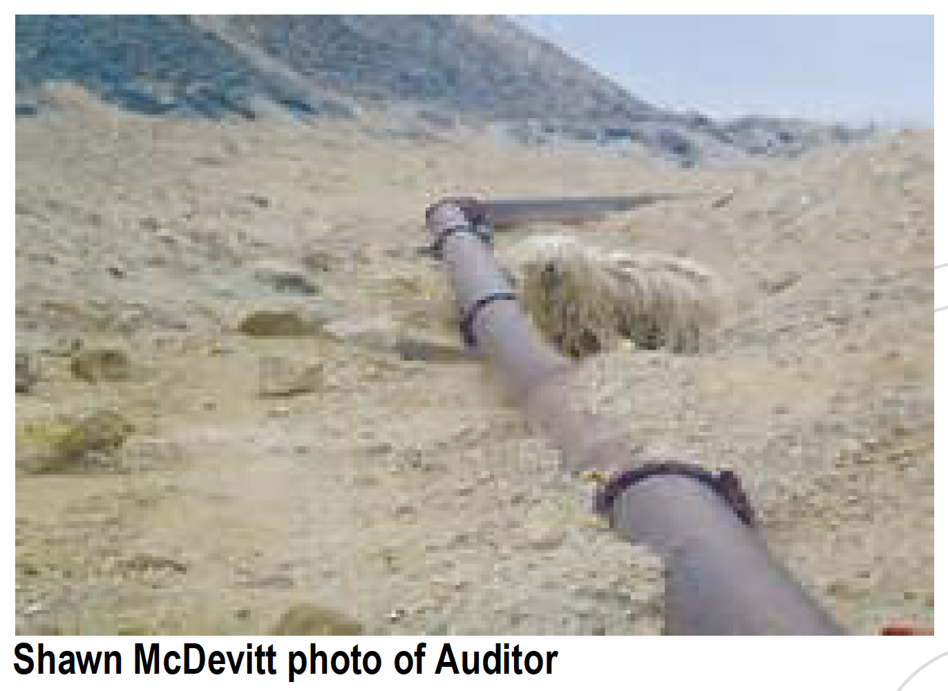 Metal pipe runs through a dry, barren landscape; the pipe is in the foreground, with hills in the background.
