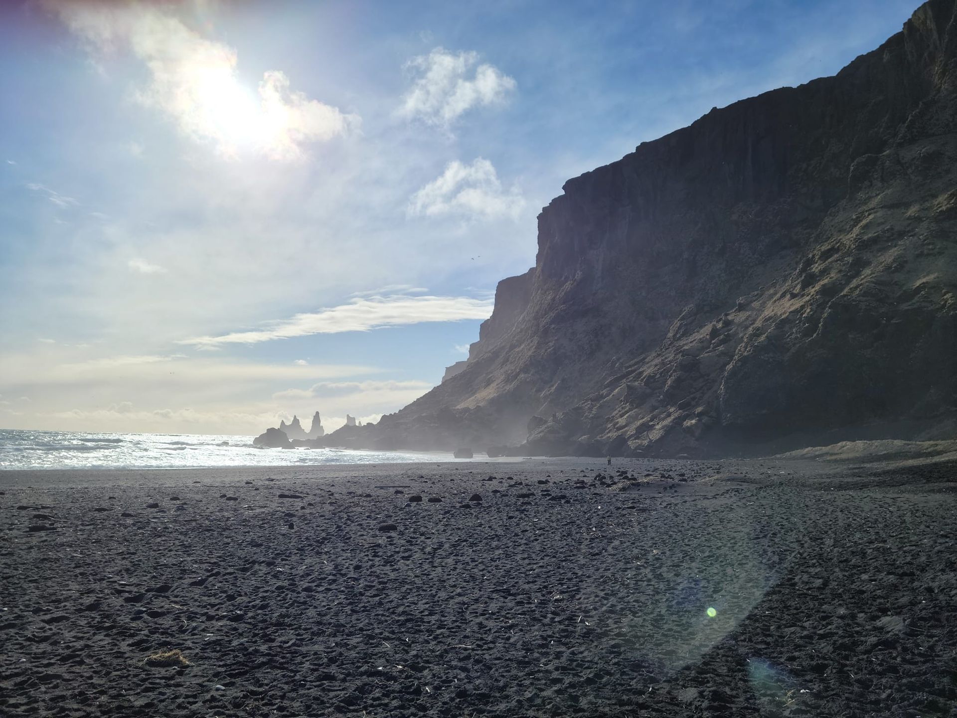 Black sand beach in the sunshine. Rocky cliffs and outcroppings can be seen in the distance.