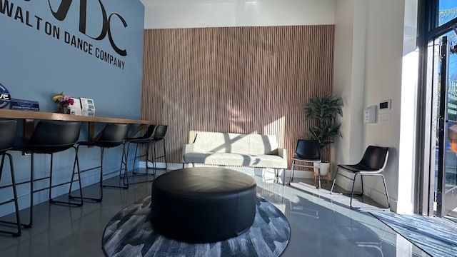 Modern lobby with stools, lounge chairs, round ottoman, striped rug, and large glass doors letting in sunlight