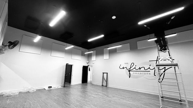Empty modern dance studio with black ceiling lights, wood floor, wall mirrors, and a ladder by the wall