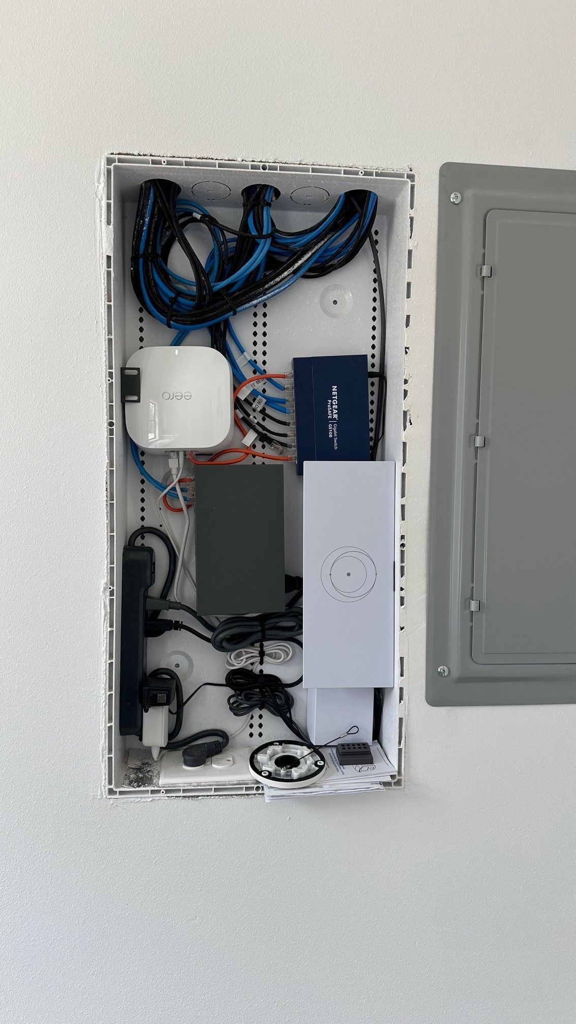 Open wall cabinet with blue network cables, router equipment, and wiring panel exposed.