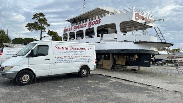 White van beside a ferry boat on a dock, with cloudy sky and water in the background