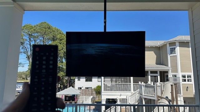 Remote control aimed at a wall-mounted TV in front of a bright backyard and pool.