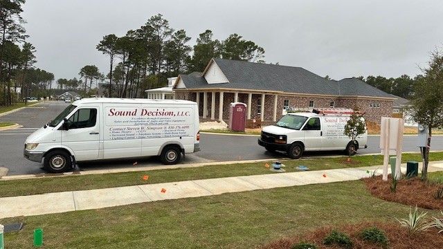 Two white service vans parked in front of a single-story brick house on a wet driveway