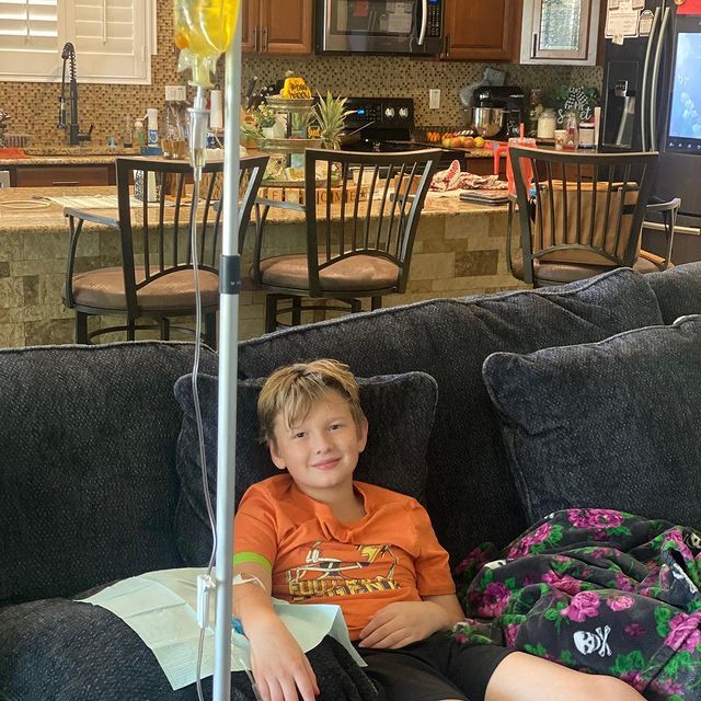 A young boy is sitting on a couch with an iv in his arm