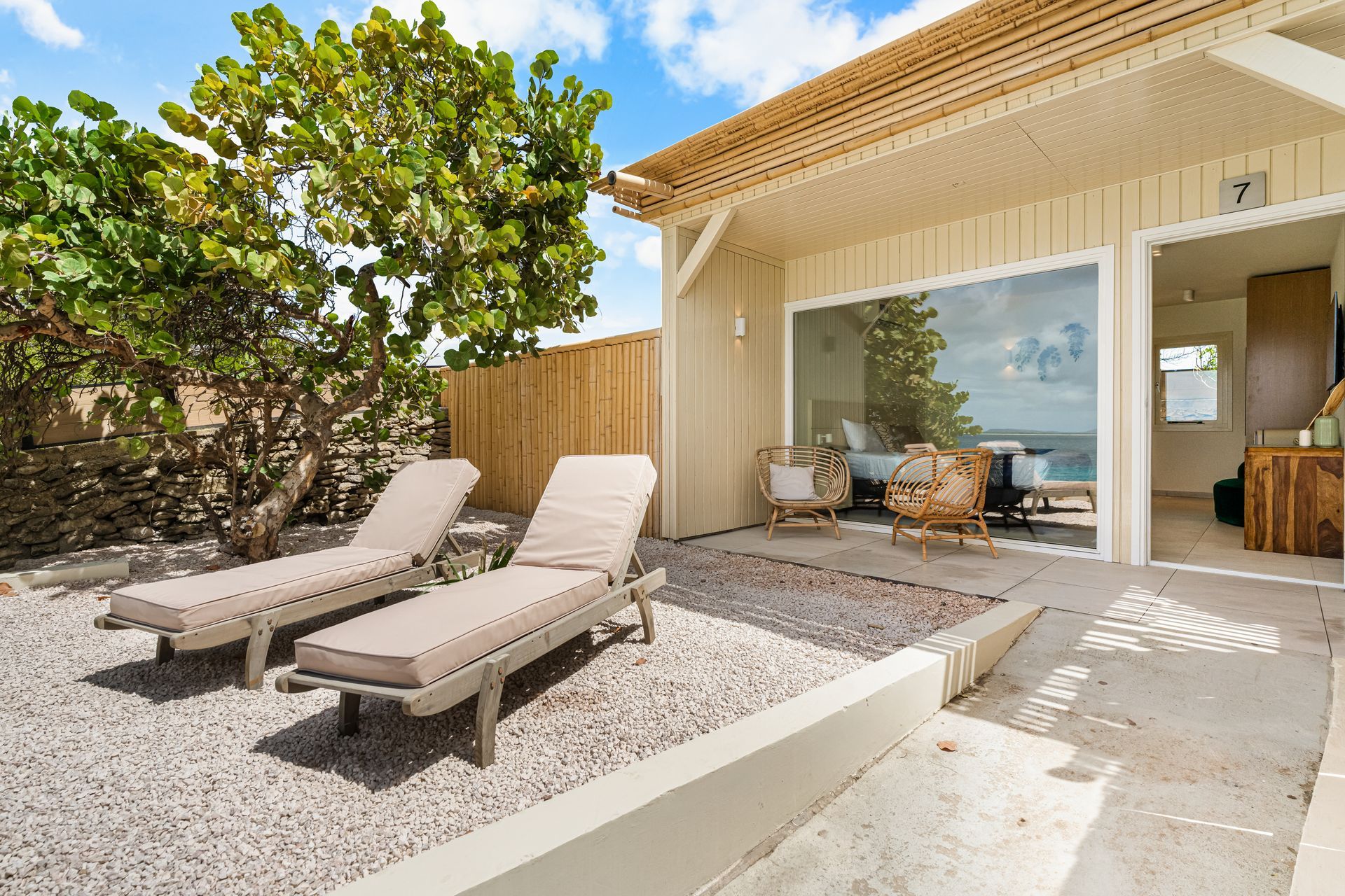 Patio with two lounge chairs, white gravel planter, and sliding glass door beside a beachside home