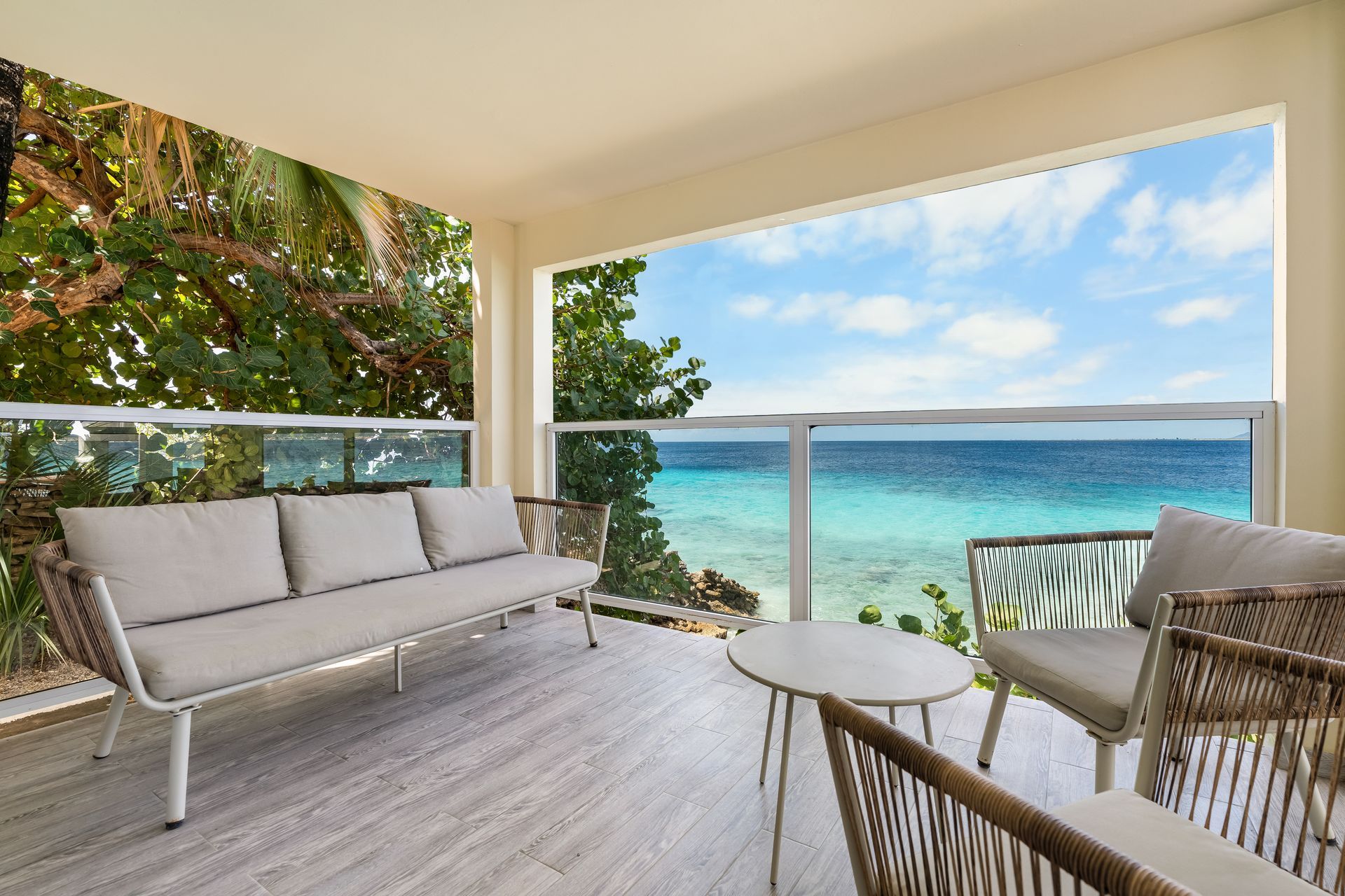 Ocean-view patio with white sofa, chairs, and a small table overlooking turquoise water