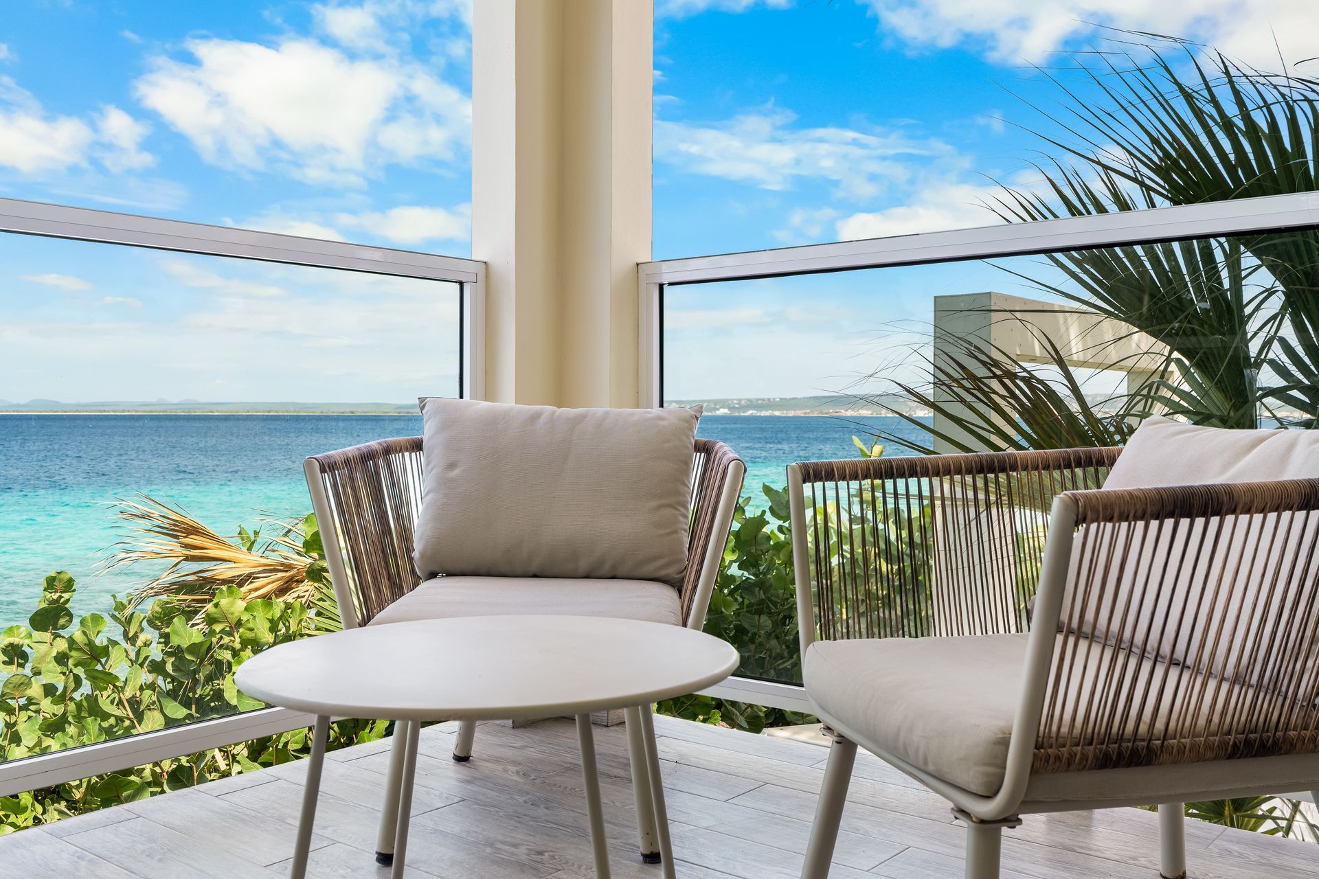 Balcony seating with ocean view, white table and chairs, palm trees, and bright blue sky