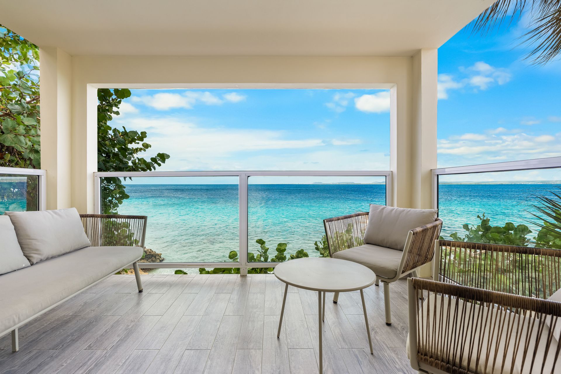 Covered oceanfront patio with white seating, small table, and turquoise sea view