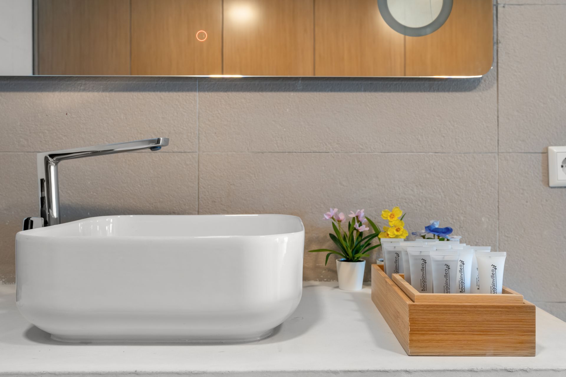 Modern bathroom sink with chrome faucet, soap dispensers, and small flowers on a countertop