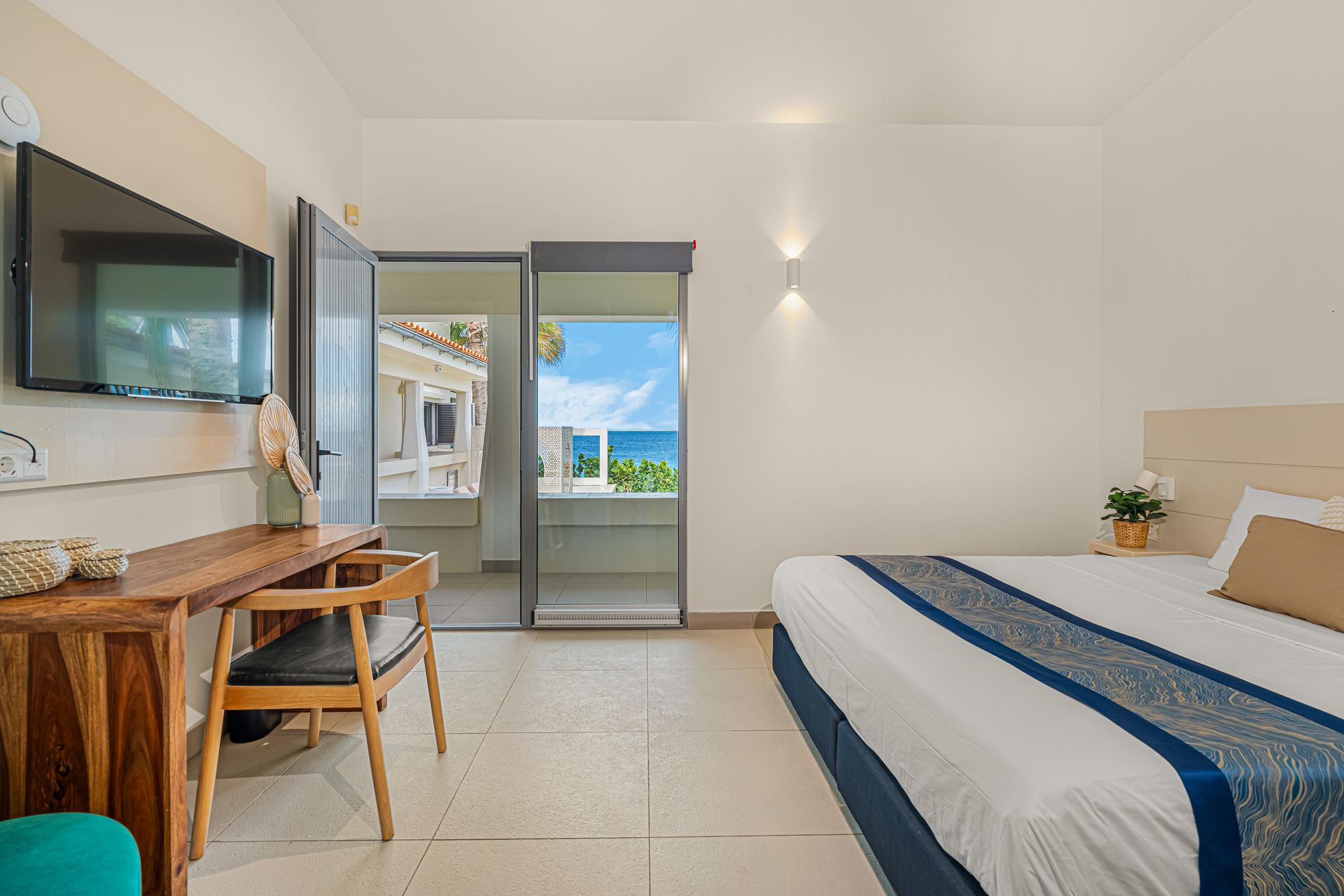 Bedroom with ocean view from open glass door, desk with TV on the wall.