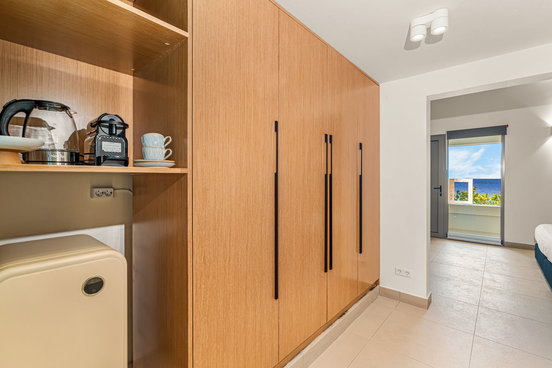 Wooden wardrobe with built-in shelves and mini-fridge in a room with a view of the ocean.