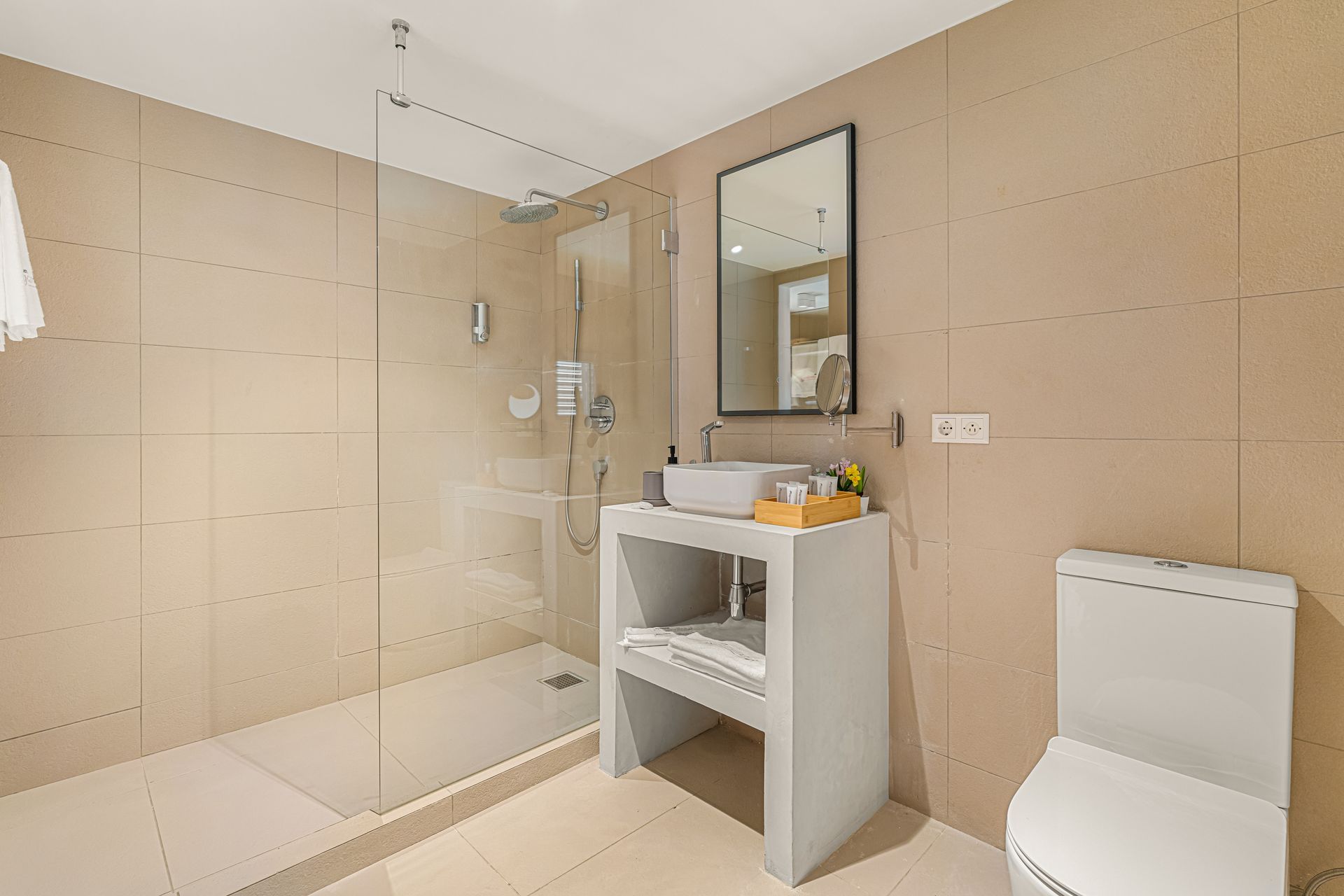 Modern bathroom with a shower, vanity, and toilet. Beige tiled walls and a glass shower door.