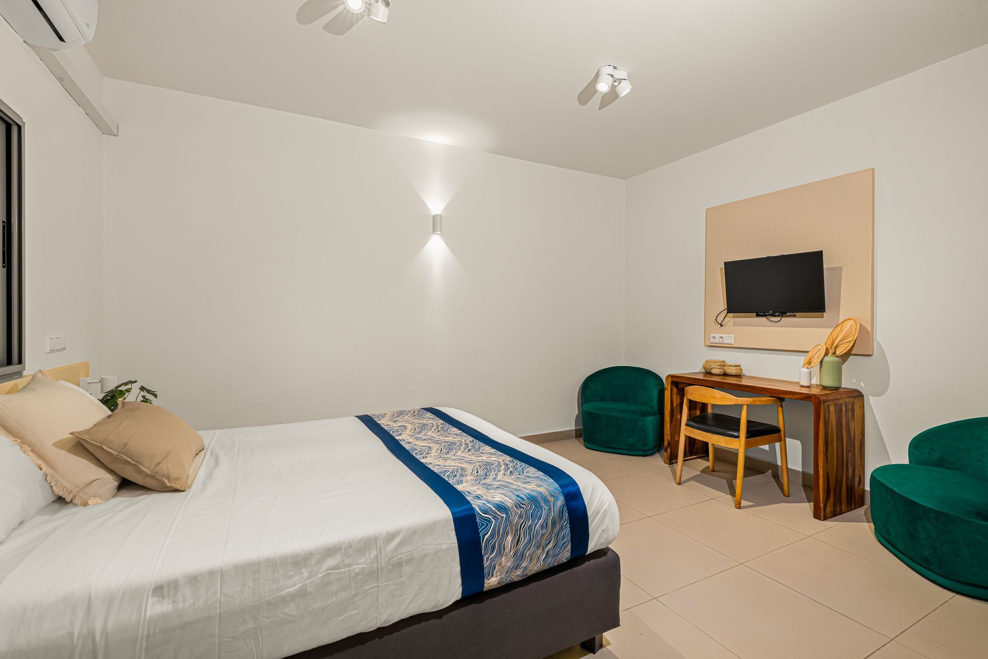 Bedroom with bed, desk, green chairs, and a TV.