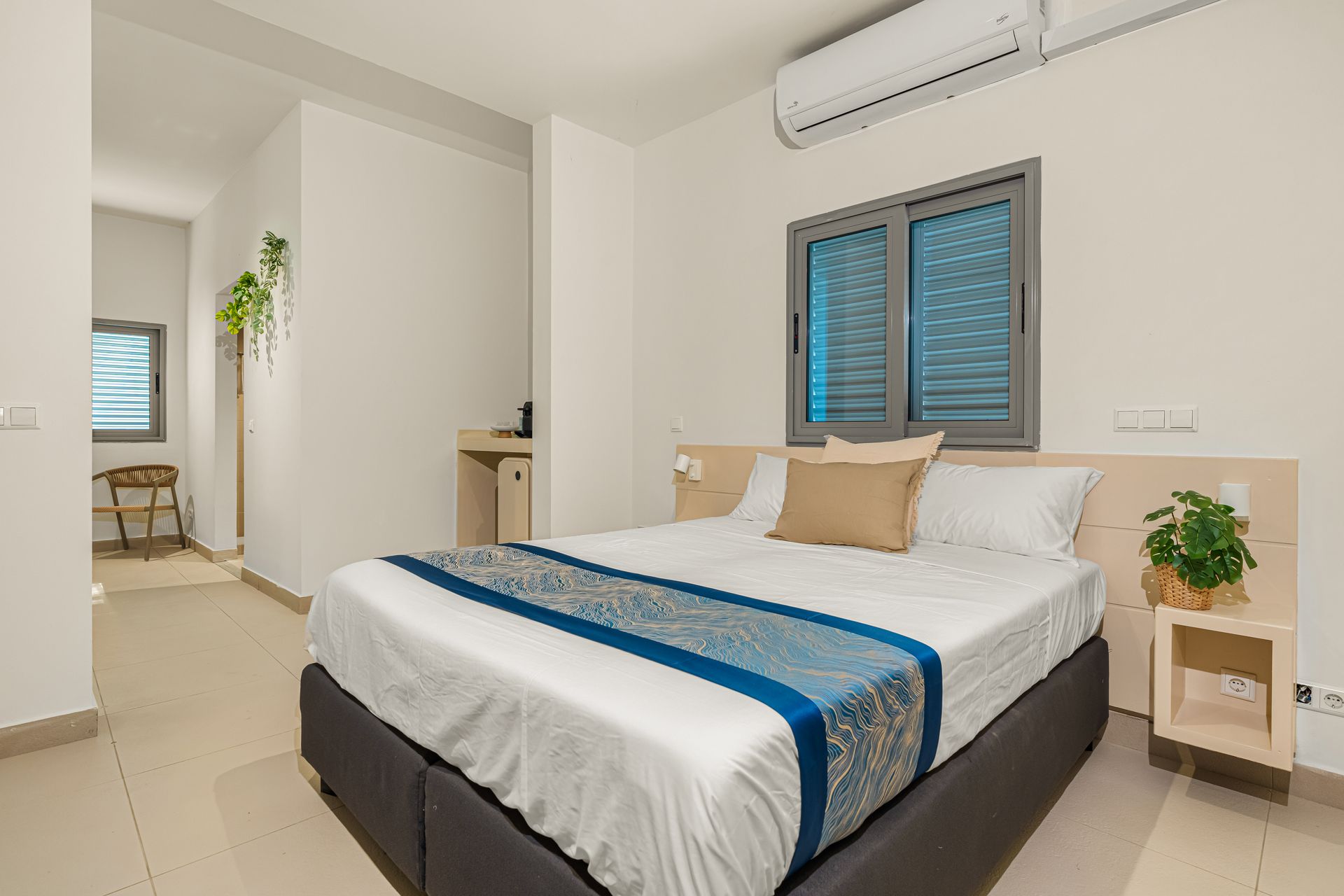 Bedroom with a bed, a window, an air conditioner, and a small table. White walls.