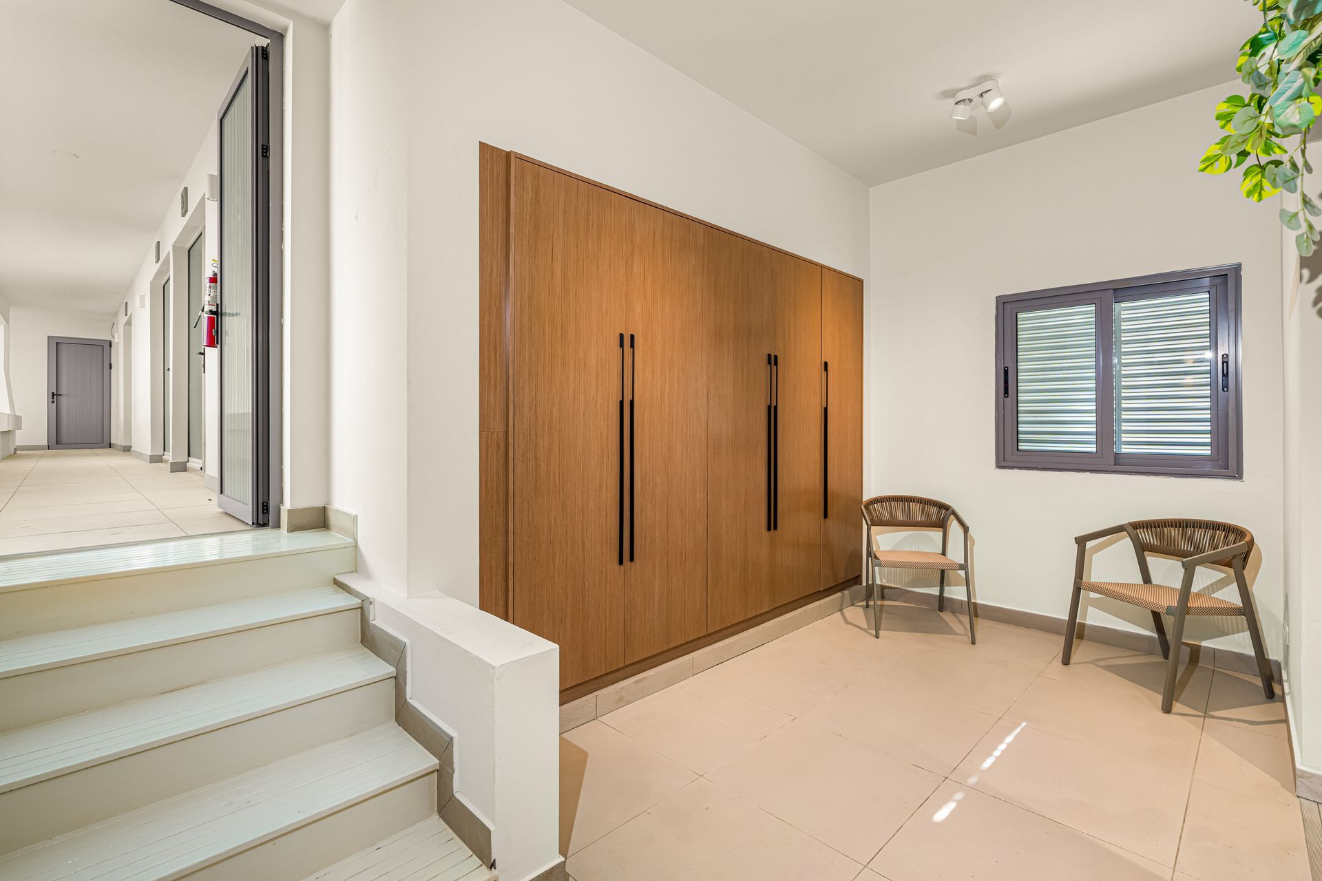 Hallway with built-in wood cabinet, two chairs, window, and stairs.