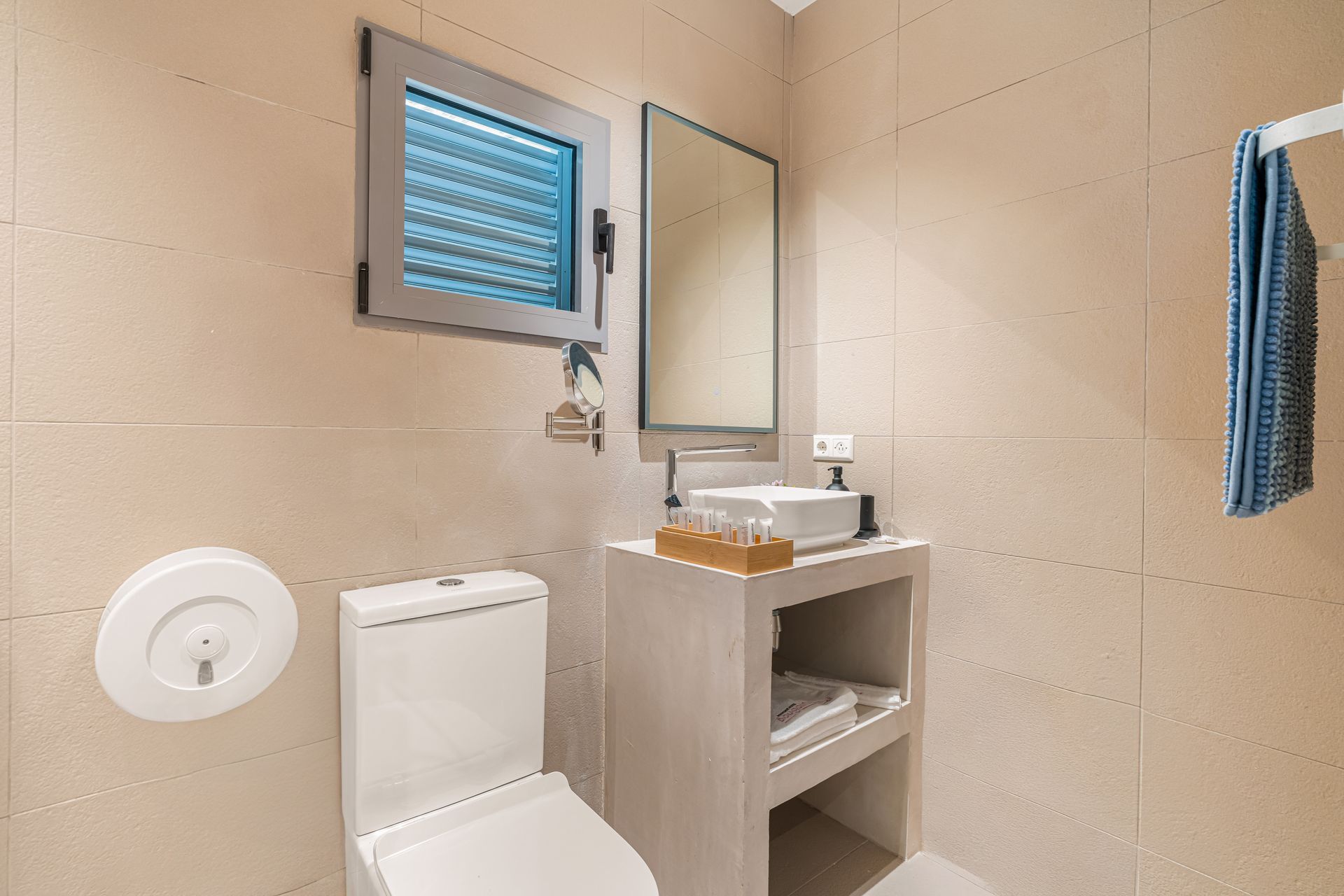 Small beige bathroom with a toilet, sink, mirror, and towel rack.