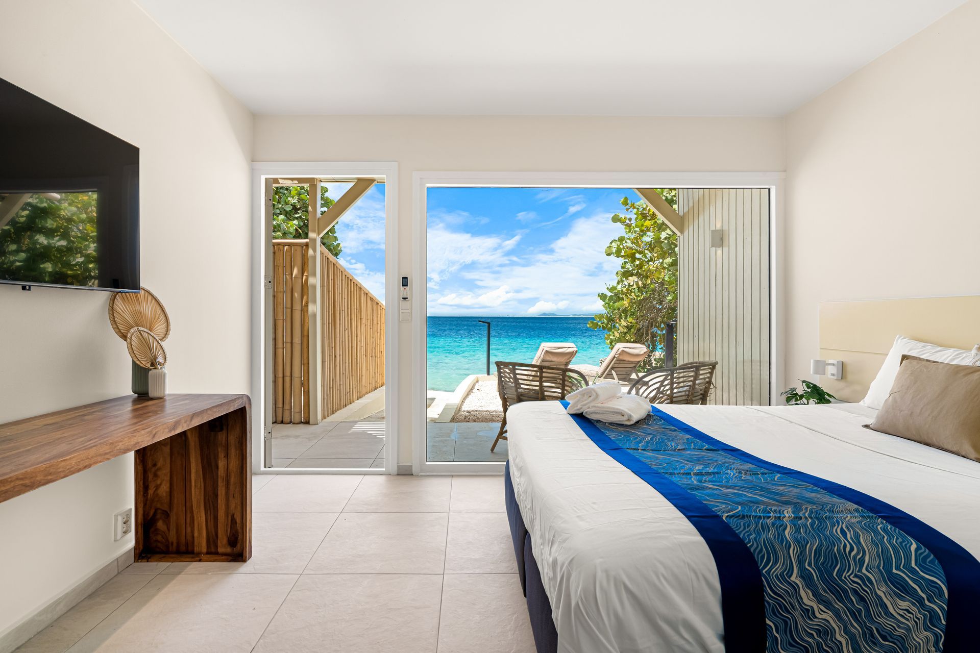 Bright bedroom with open doors to a tropical beach and ocean view