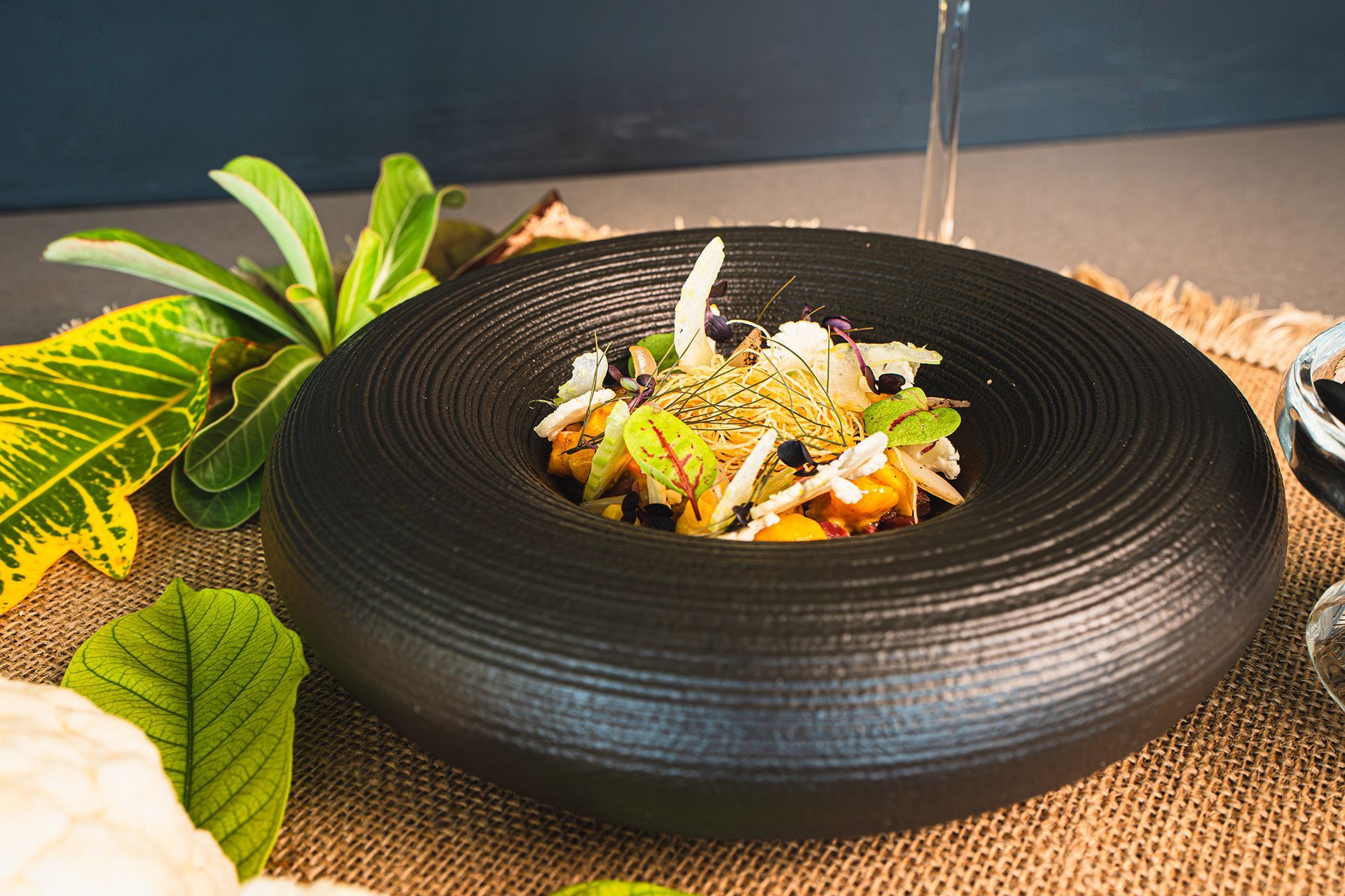 Black bowl with food, decorated with leaves and herbs on a textured surface.