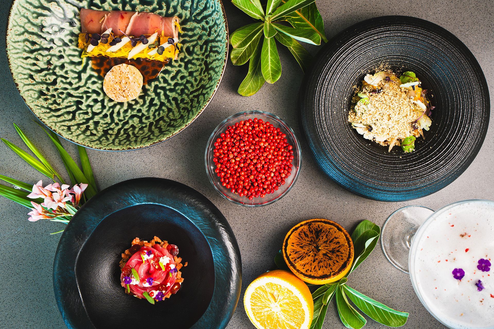 Arrangement of gourmet dishes on a gray surface, featuring colorful food presentations, including caviar and drinks.