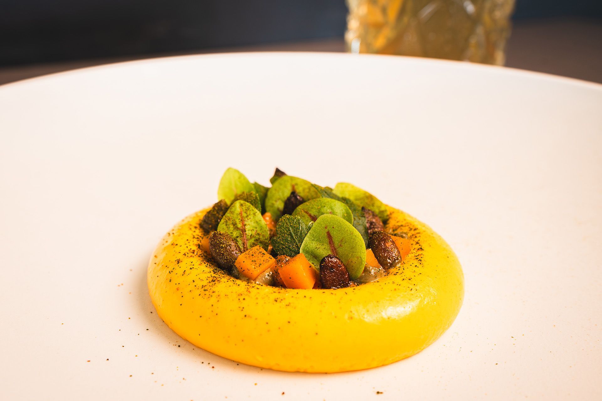 Yellow vegetable puree ring topped with mixed greens and vegetables on a white plate.