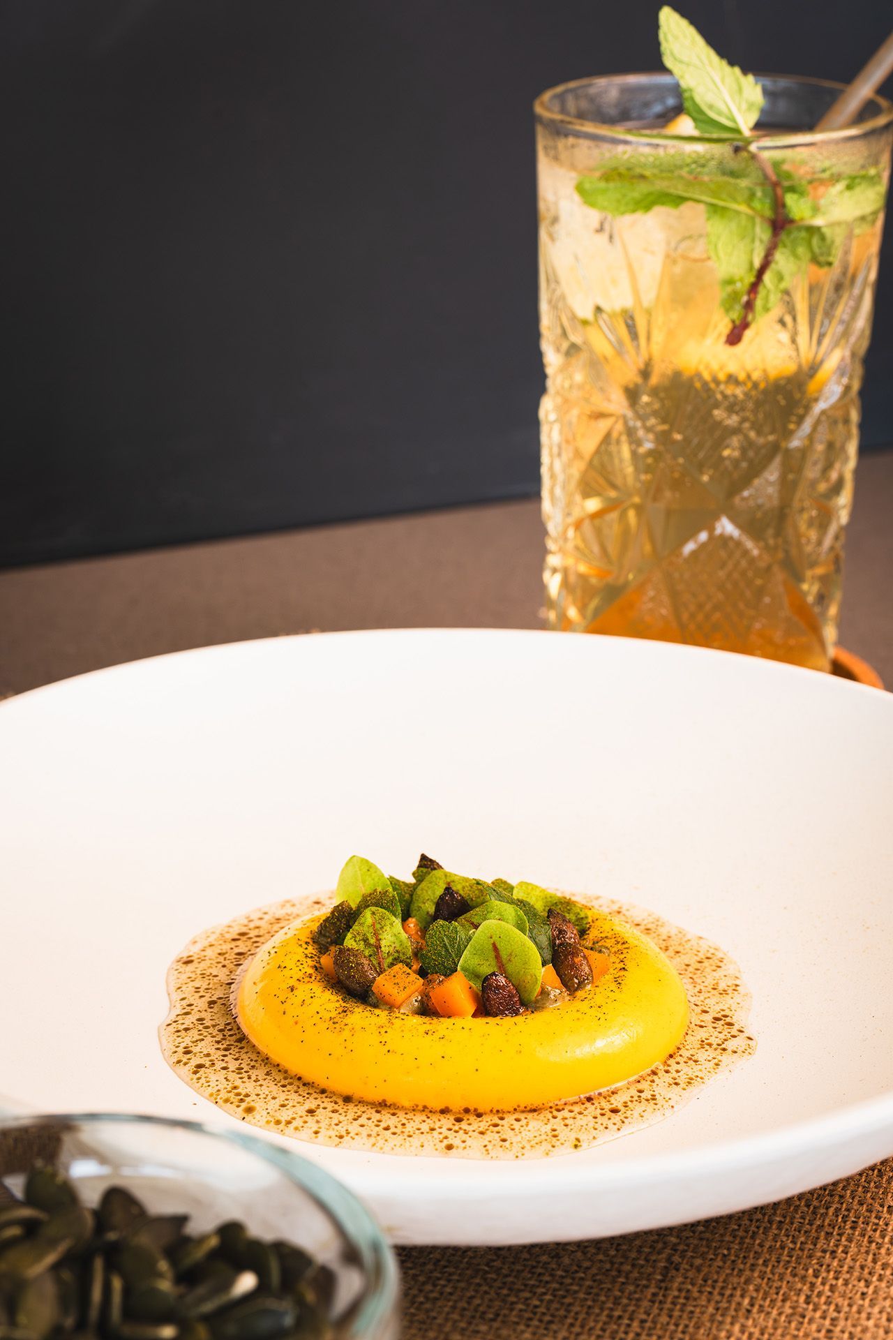 Yellow dessert on a white plate with a drink in the background, garnished with mint.