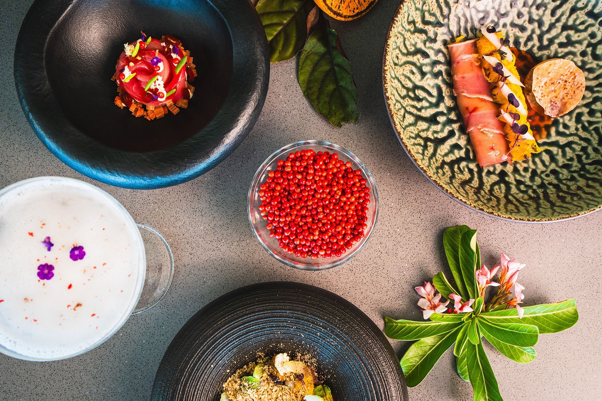 Overhead view of several small dishes with colorful food and ingredients, artfully arranged on a gray surface.
