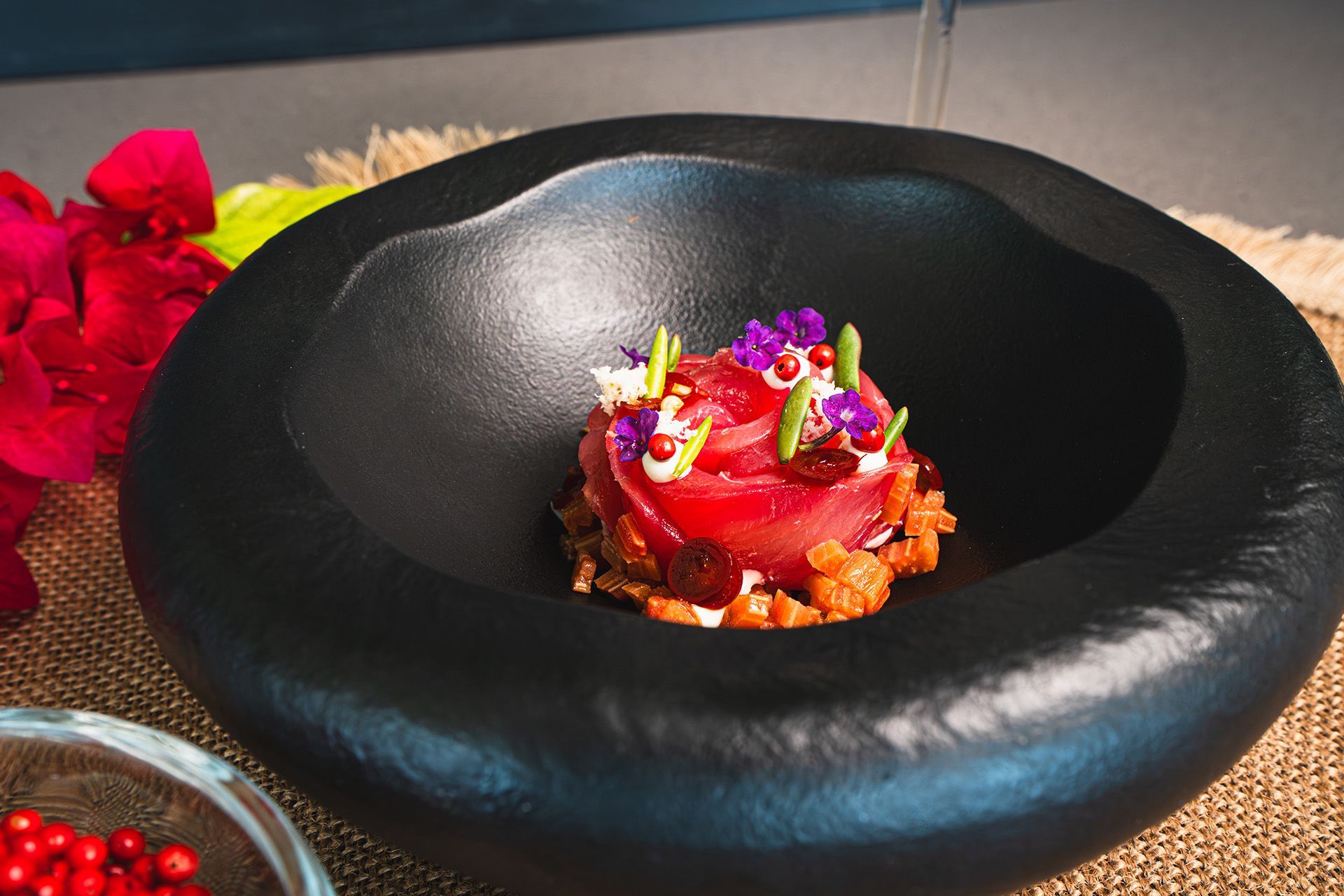 Tuna tartare in black bowl, garnished with flower petals, pistachio and pomegranate seeds.