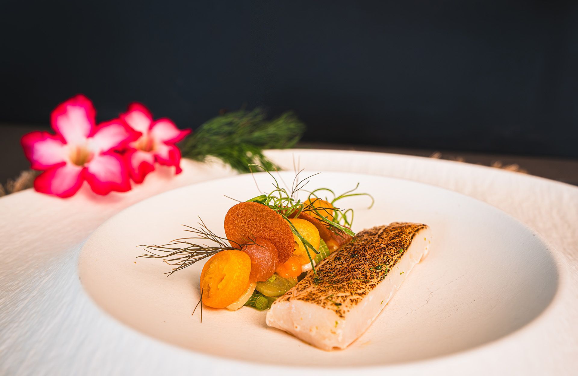 White plate with fish, vegetables, garnish, and a pink flower.
